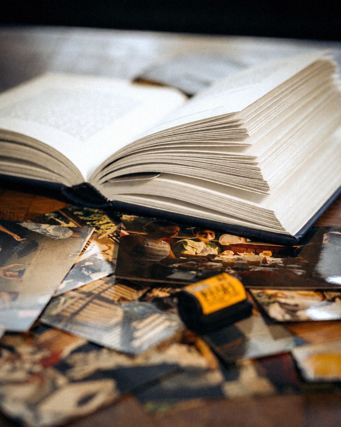 Un livre ouvert entouré de vieilles photographies et d'une pellicule, sur une table en bois.